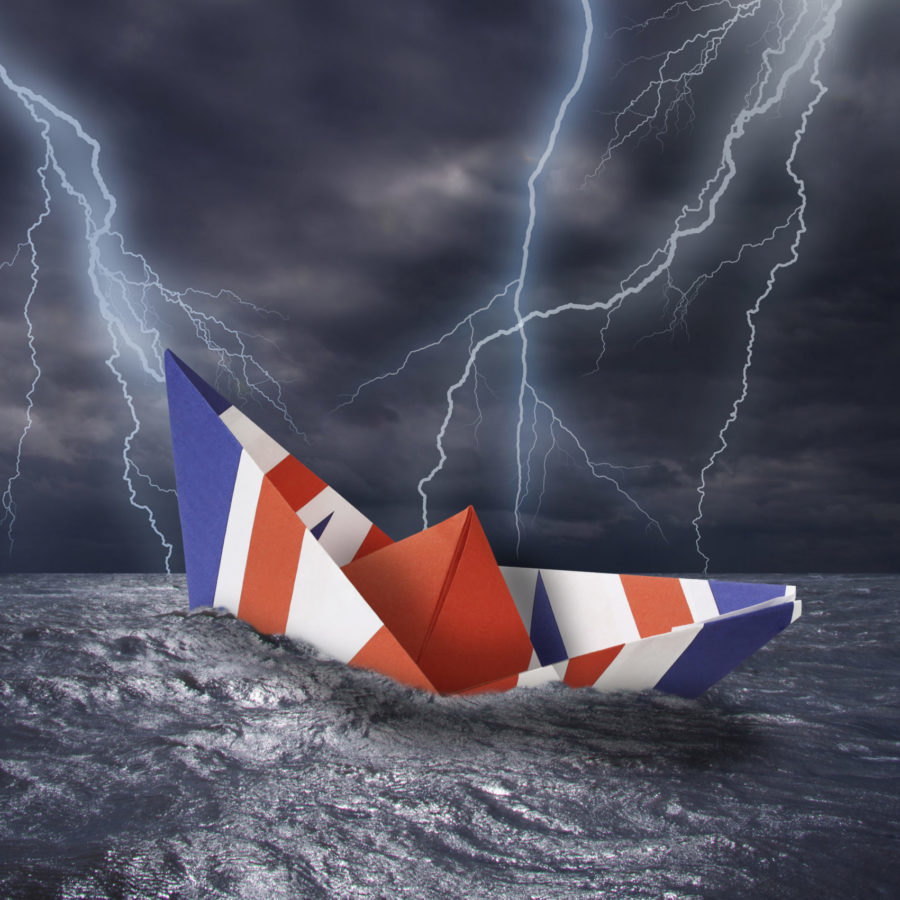 UK paper boat made as the flag of the United Kingdom almost capsizes in high waves. Bolt of lightning i stormy dark sea weather during a thunder-storm with dramatic cloudscape.