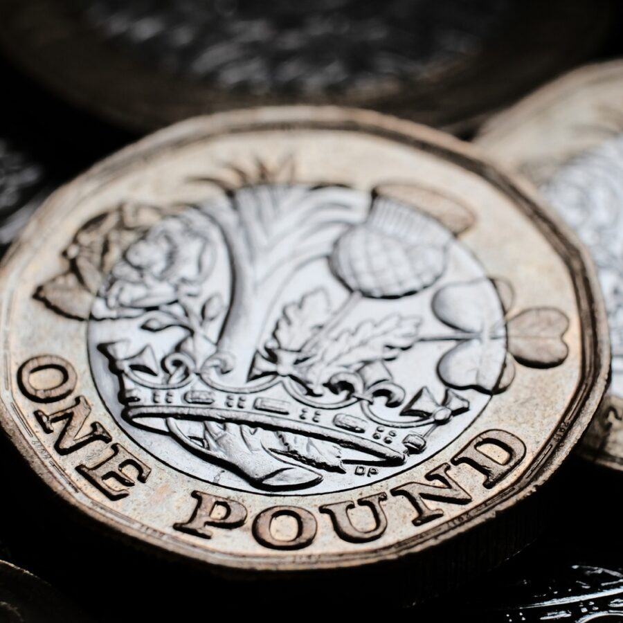 British one pound coins placed on top of each other in the box. Coins have shiny reflections and deep shadows.
